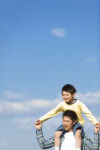 Father carrying his young son on his shoulders against a blue sky